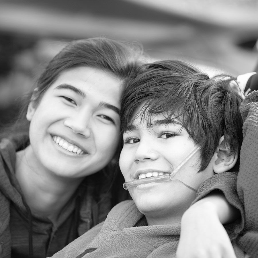 close up asian youngsters. girl has her arm around boy, who is wearing a device to aid him with his disability