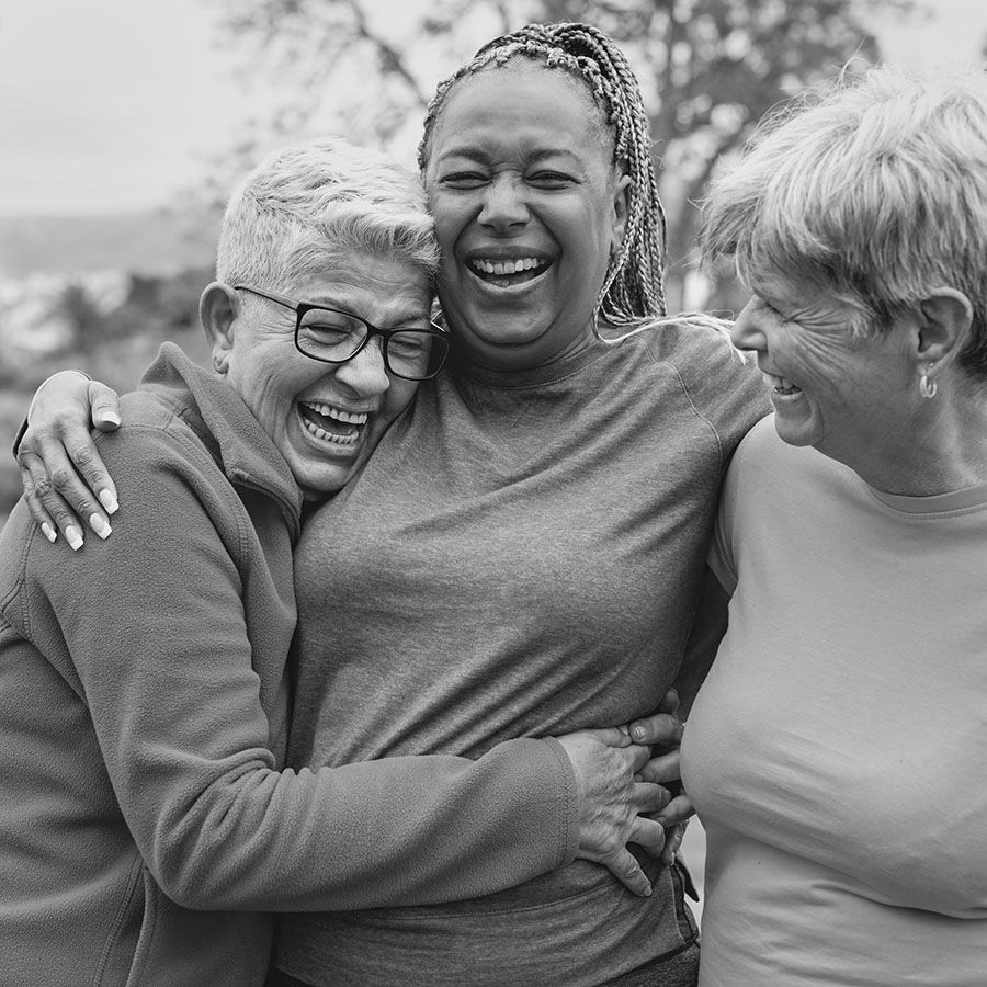 close up of three middle-aged women laughing and embracing embracing