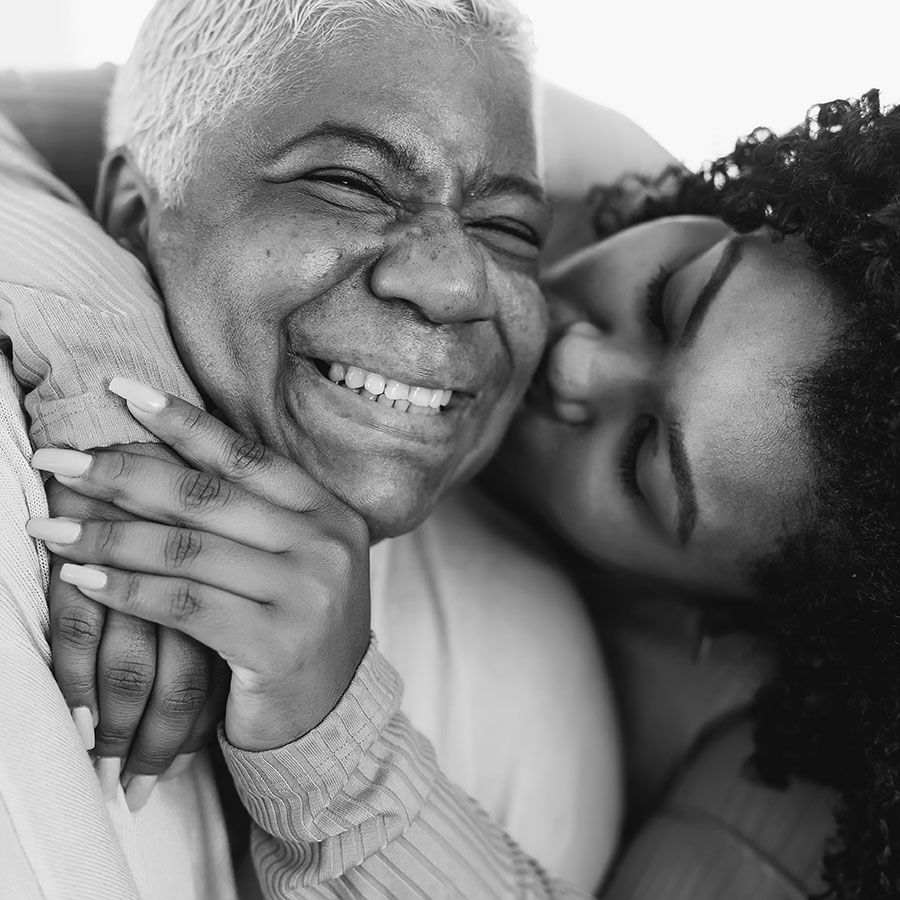 young african-american woman embracing and kissing an older african-american woman. both are smiling.