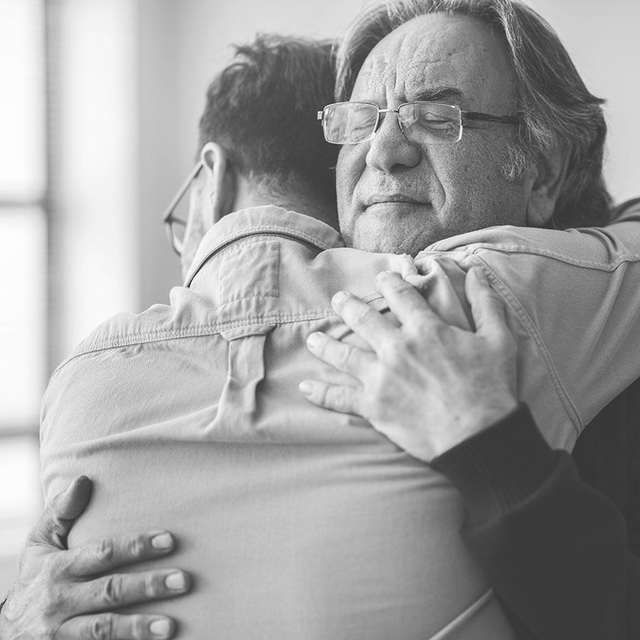 two men hugging. older man has his eyes closed
