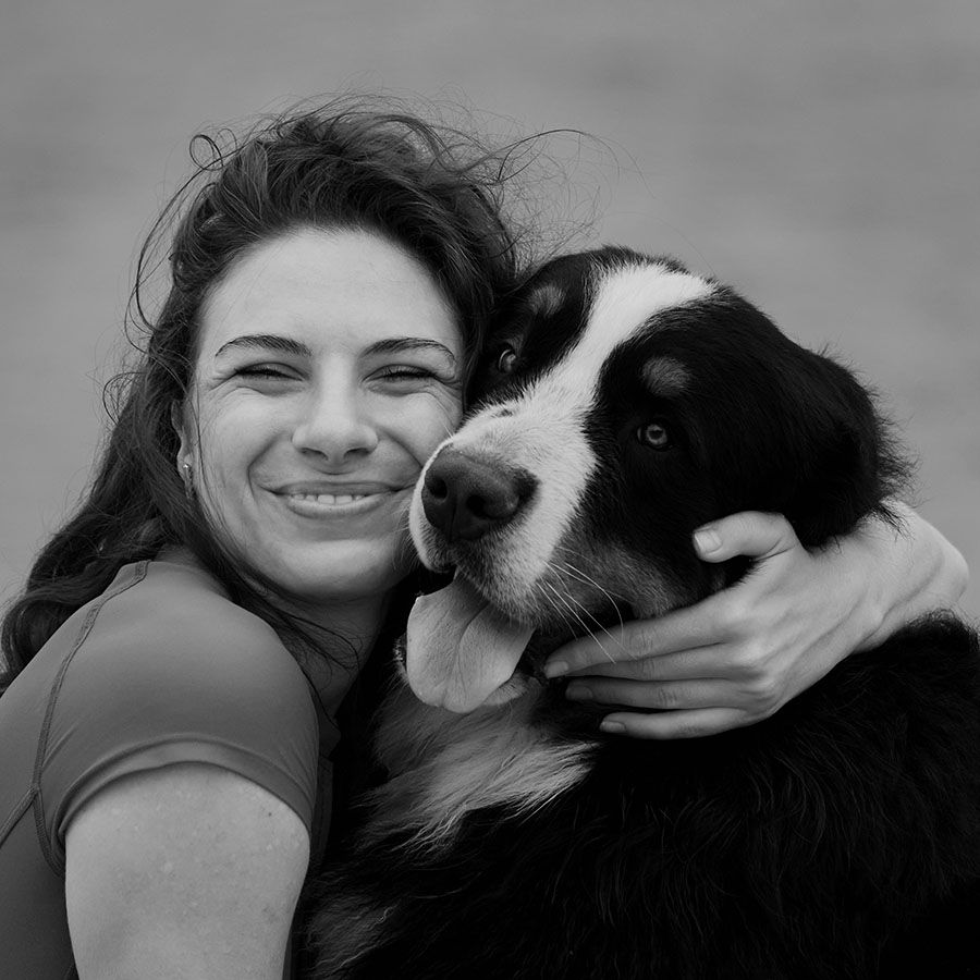 smiling woman in red shirt embracing her bernese mountain dog